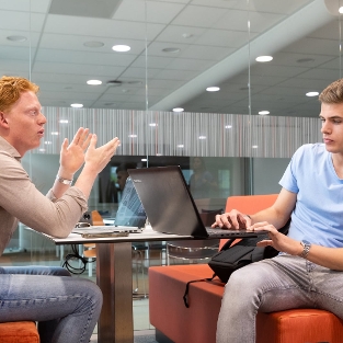 2 studenten zitten achter hun laptop en zijn samen in gesprek