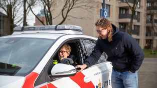 Een politieagent zit in de auto en praat met een andere persoon die naast de politieauto staat